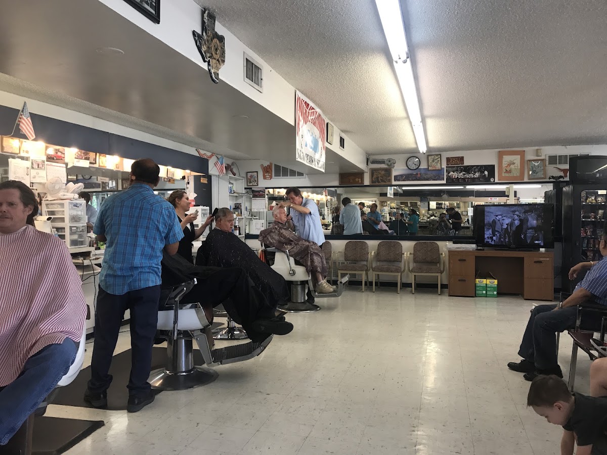 Busy interior of Adolph's Barber Shop with several barbers cutting hair and customers waiting